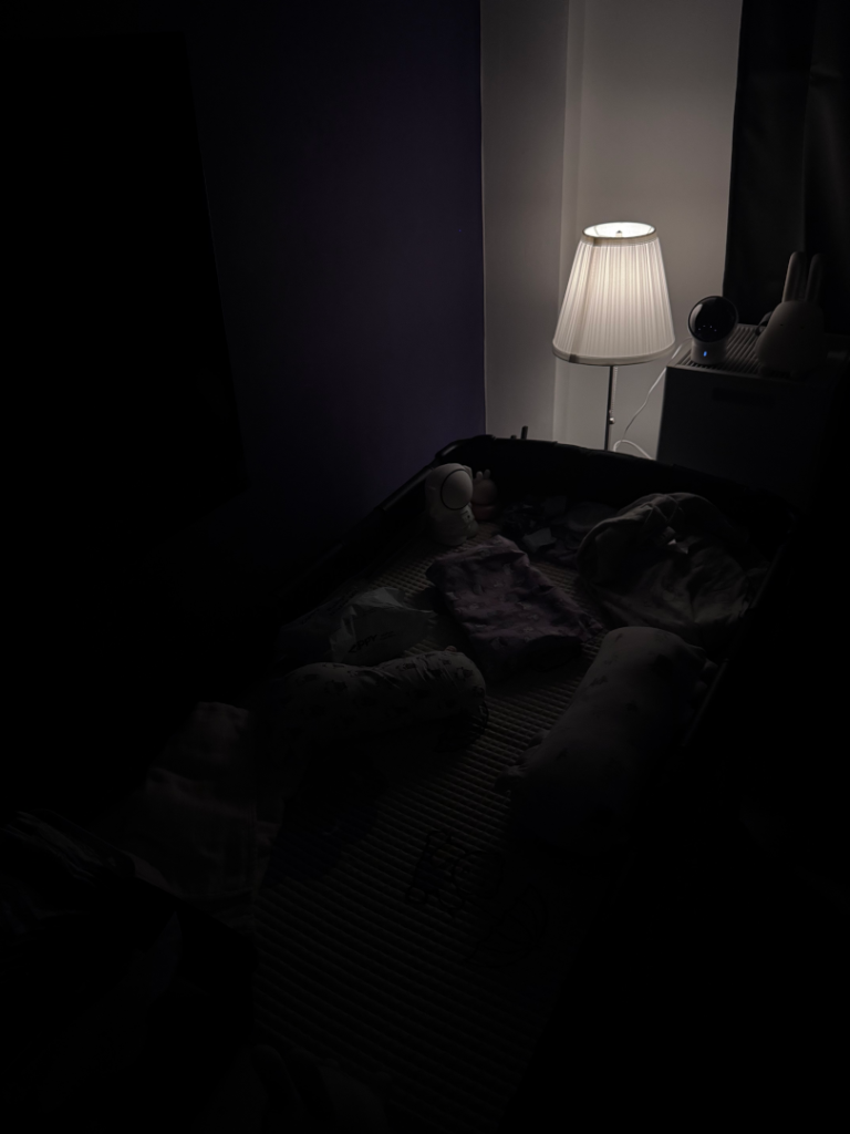 Baby night light setup with an IKEA Årstid lamp and Tapo L530E smart bulb dimmed low beside a baby cot in a dark room