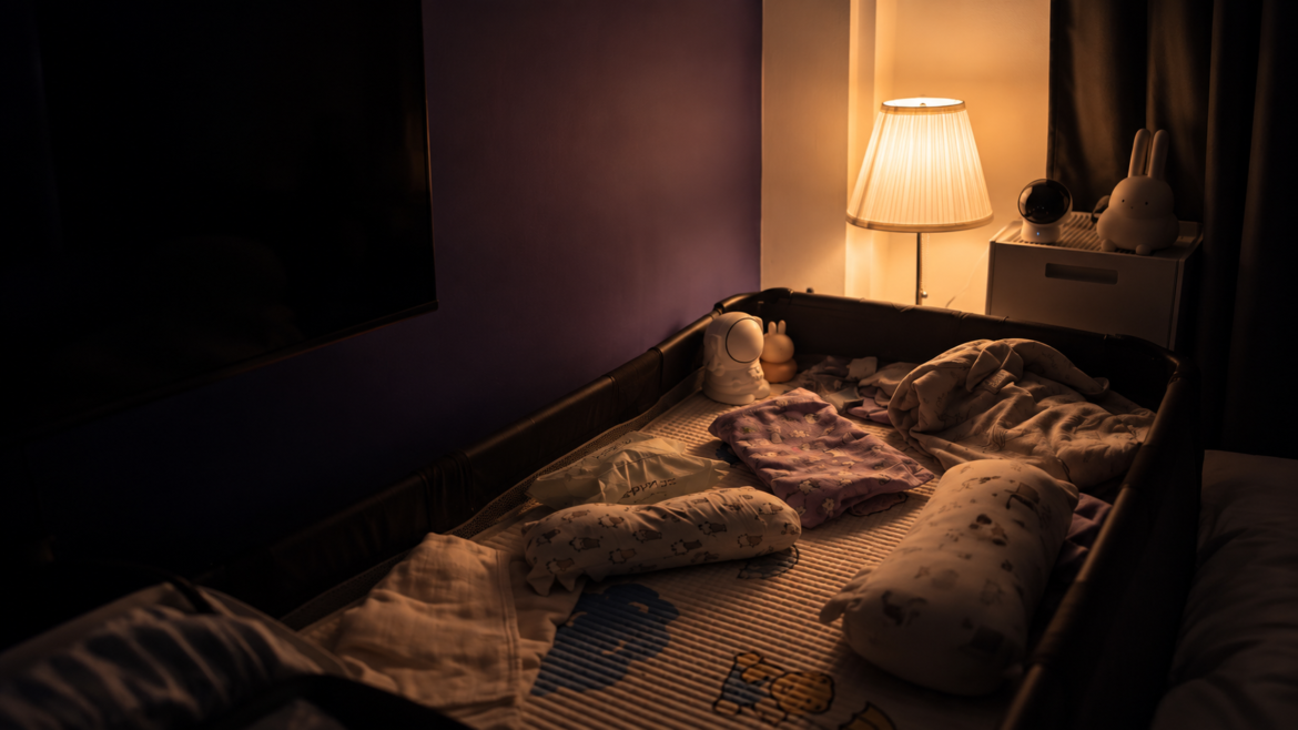Baby night light setup with a warm glowing IKEA Årstid lamp and Tapo L530E smart bulb beside a baby cot in a dark bedroom
