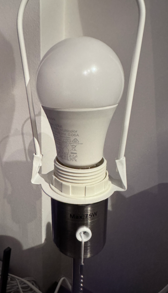 Tapo L530E multicolour smart Wi-Fi bulb screwed into the E27 socket of an IKEA Årstid table lamp with pull switch