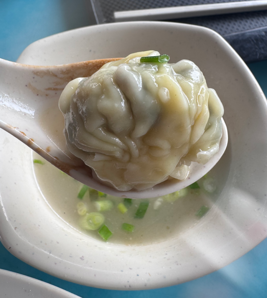 Close-up of a large, plump wanton on a spoon at Chef Kang’s Noodle House, showing its size against the soup spoon