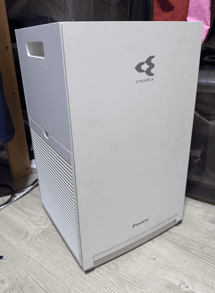 A white Daikin MC30YVM7 air purifier with the Streamer logo on the front, standing on a wooden floor in a bedroom.