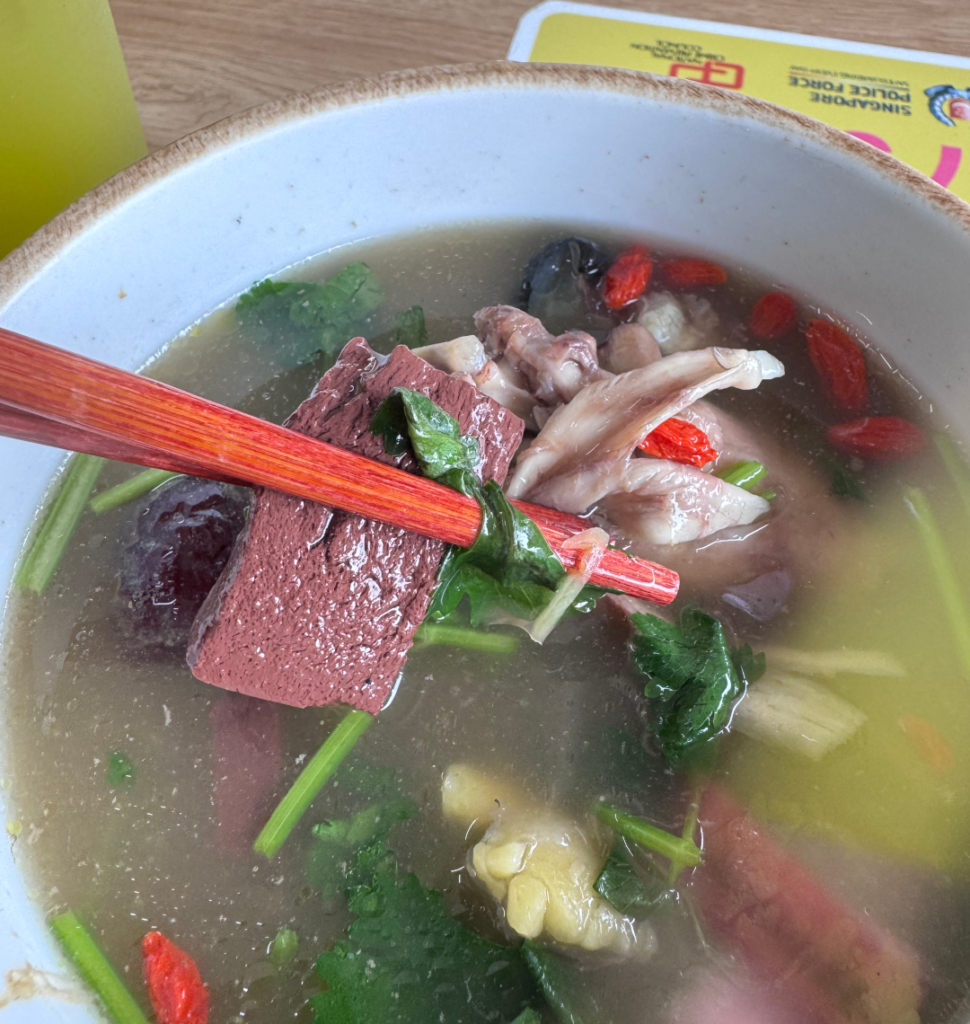 Piece of pig’s blood held up with chopsticks over turtle soup with wolfberries and coriander