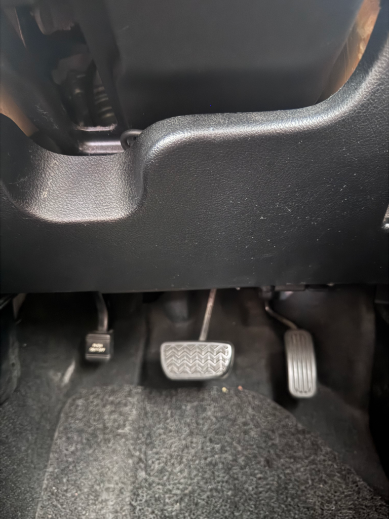 Driver’s footwell and pedals in a Tribecar Toyota Sienta Hybrid. This is where you can find the manual parking lever.