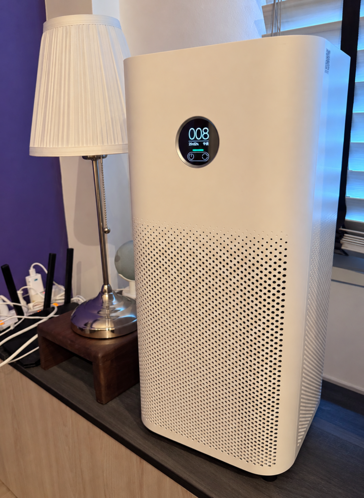 A Xiaomi Air Purifier 4 on a bedroom cabinet beside an IKEA Årstid lamp. Its round display shows a PM2.5 reading of 8, a temperature of 29°C and humidity of 62%.