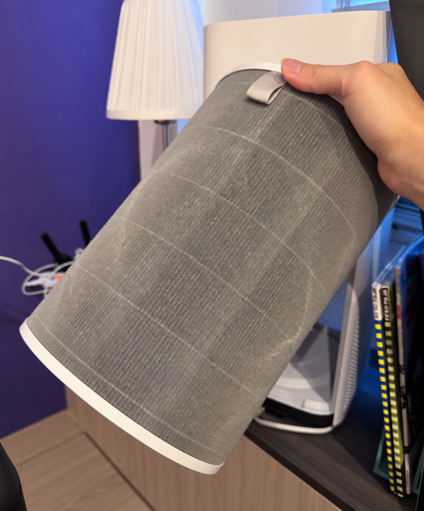 A hand holding the tall, grey cylindrical filter from a Xiaomi Air Purifier 4, with its fine mesh outer layer wrapping all the way around.